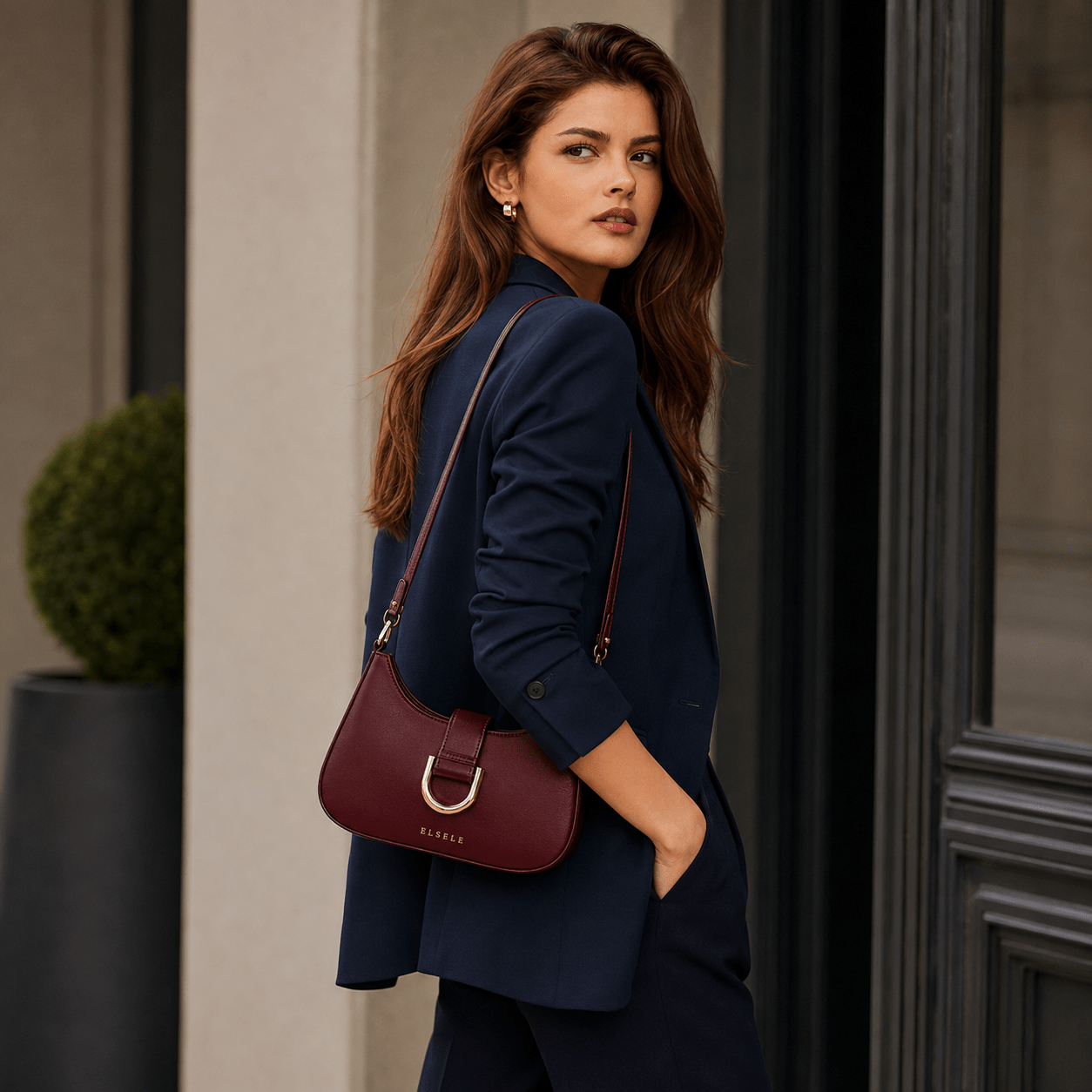 ELSELE Bordeaux Schultertasche mit dunkelblauem Blazer Frau trägt eine bordeauxrote ELSELE Schultertasche zu einem dunkelblauen Blazer